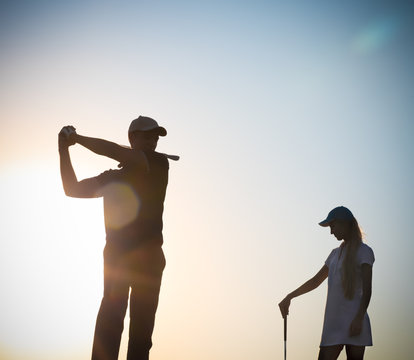 Male And Female Golfers At Sunset