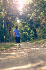 Athletische junge Frau läuft im Wald, Blick von hinten