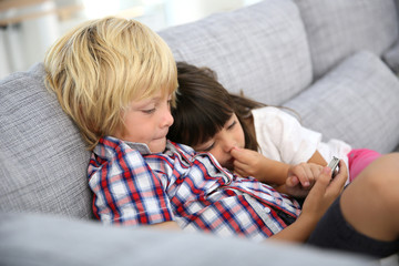 Fototapeta premium Kids sitting in sofa and playing with smartphone
