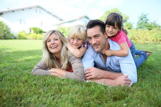 Family of four laying on grass in front of house