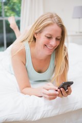 Happy blonde using smartphone on bed
