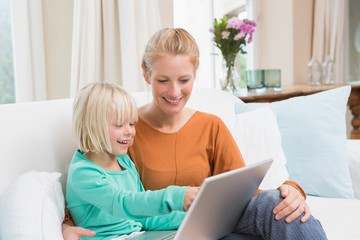 Happy mother and daughter on the couch using laptop