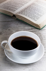 Cup of coffee and old book on a wooden table