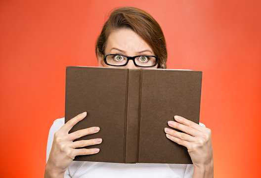 headshot woman with glasses hiding face behind book monitoring 