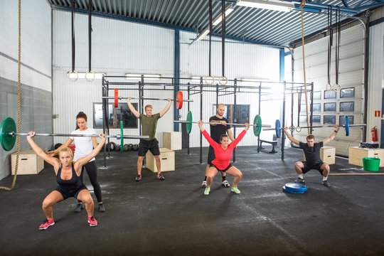 Trainers Assisting Athletes In Exercising With Barbells