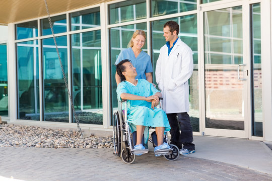 Nurse And Doctor Looking At Patient On Wheelchair Outside Hospit