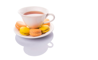 A cup of tea and yellow and orange colored macarons 