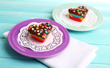 Delicious rainbow cakes on plates, on color wooden background