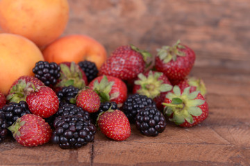 Ripe apricots and berries on wooden background