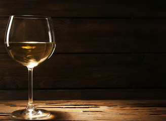 Goblet of white wine on wooden table on wooden wall background
