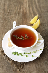 Cup of tasty herbal tea with thyme and lemon, on wooden table