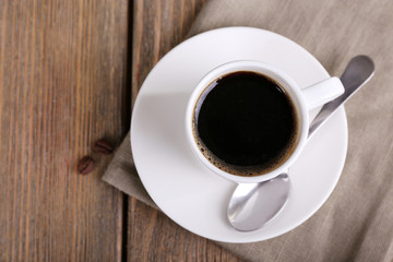 Cup of coffee and coffee beans on napkin on wooden background