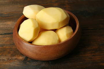 Raw peeled potatoes in bowl  on wooden background
