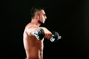 Fototapeta na wymiar Portrait of a sportsman lifting dumbbells over black background