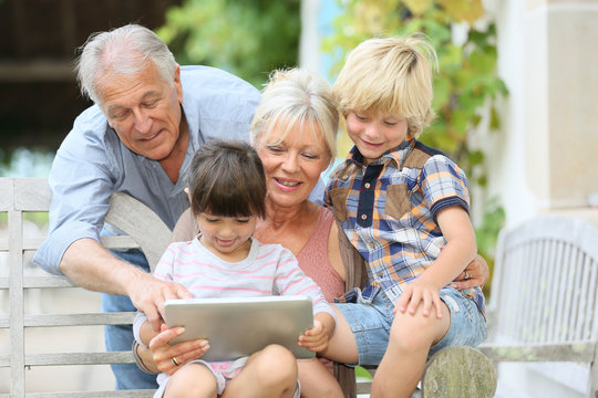 Happy grandparents playing game on tablet with kids