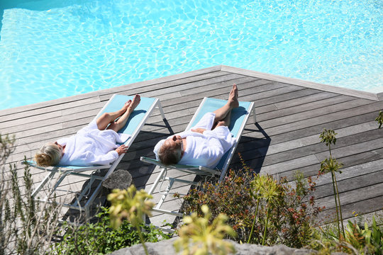 Senior Couple Relaxing By Swimming Pool In Spa Hotel