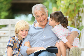 Senior man reading book with grandkids - obrazy, fototapety, plakaty