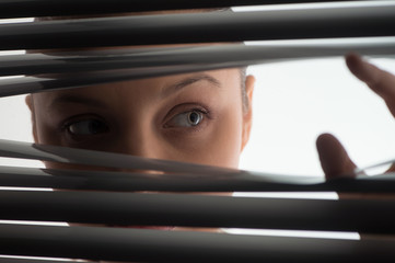 young woman peeking through closed blinds or shutters.