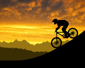 Obraz premium silhouette of the cyclist on downhill bike at sunset
