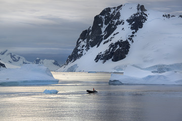 People in small inflatible zodiac rib boats passing icebergs and ice floes on the calm water around small islands of the Antarctic Peninsula.