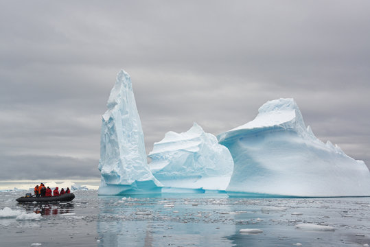 People in small inflatible zodiac rib boats passing towering sculpted icebergs on the calm water around small islands of the Antarctic Peninsula.