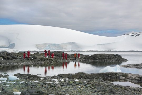Travellers in bright orange waterproofs observing and photographing the scenery and wildlife on an Antarctic island.