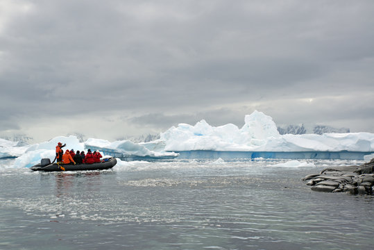 People in small inflatible zodiac rib boats passing icebergs and ice floes on the calm water around small islands of the Antarctic.