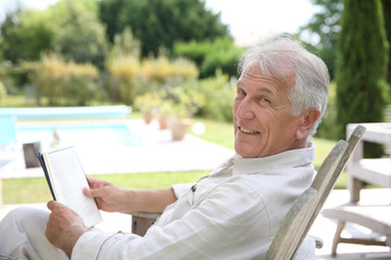 Senior man reading book in pool deck chair