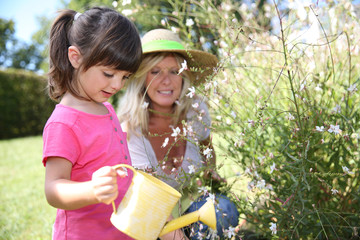 Woman with little girl watering plants in garden