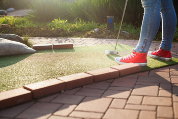 Young woman plays adventure/mini golf in summer evening