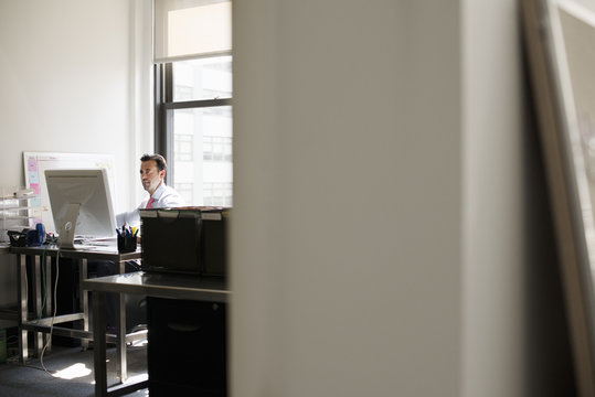A man seated at a desk in an office, using a computer.