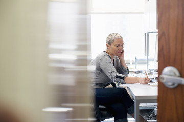 A woman working in an office alone. Focusing on a task, making notes with a pencil.