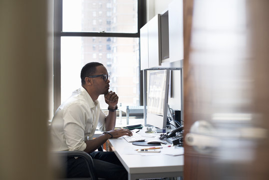 A man working in an office seated at a desk. Looking at a computer screen.