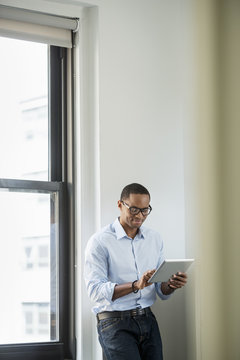 A businessman using a digital tablet, standing by a window.