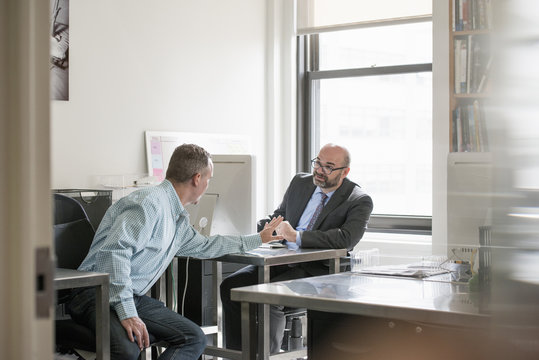 Office life. Two men seated talking to each other.