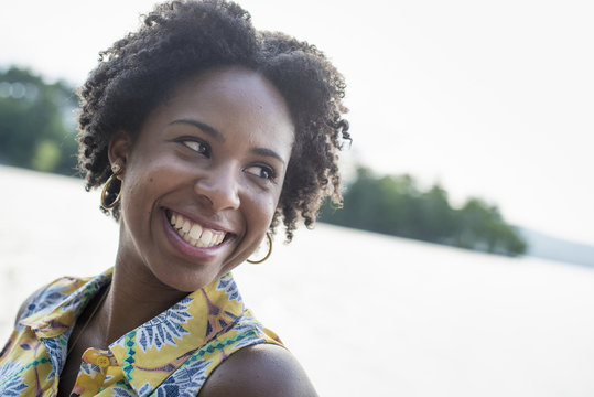 A woman smiling and laughing on a lake shore.