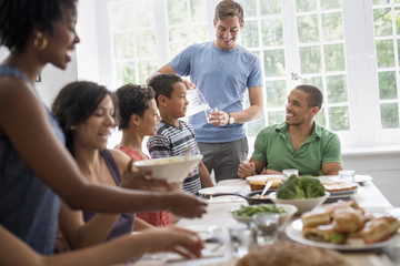 A family gathering; men; women and children around a dining table sharing a meal.