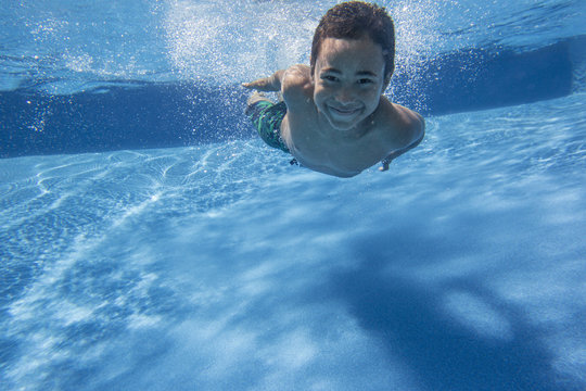 A boy swimming underwater smiling at the camera.