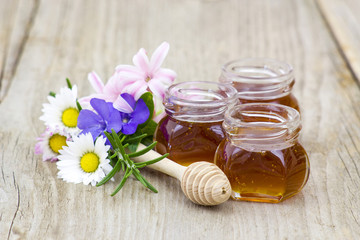 Fototapeta na wymiar Honey in jars, flowers and honey dipper on wooden background