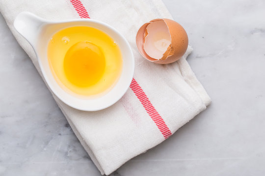 one egg yolk in white bowl and broken egg shells