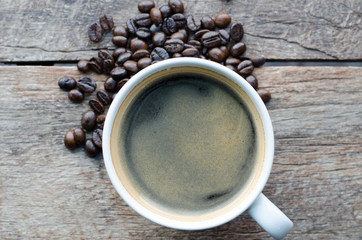 white cup of black coffee with beans on wood table top view