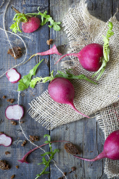 raw whole and sliced radishes on burlap on rustic wooden table