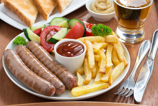 lunch with grilled sausages, French fries, vegetables and beer