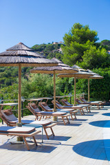 Wooden deck chairs and umbrellas near infinity pool in luxury