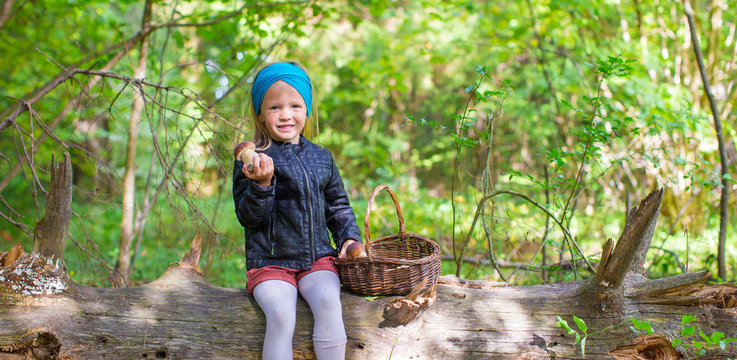 Little adorable girl gathering mushrooms in an autumn forest
