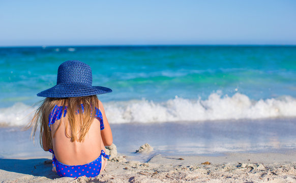 Rear view of adorable little girl in big blue straw hat at white