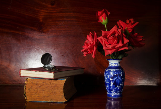 Artificial rose in vase with watch and book.