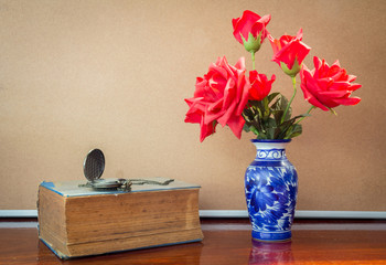 Artificial rose in vase with watch and book.