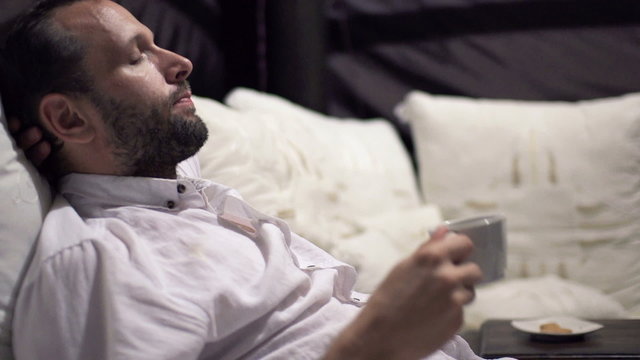 Young Man Drinking Coffee And Relaxing On Bed