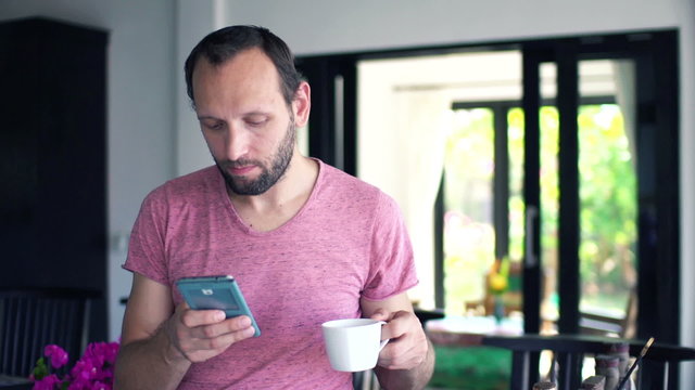 Young man sending sms on smartphone, drinking coffee at home